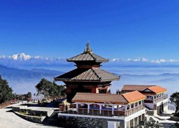 A stunning view of a traditional Nepali temple with a multi-tiered brown roof and a white and brown building in the foreground, set against a backdrop of snow-capped mountains and a clear blue sky.