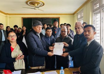 Mayor Baldev Singh Gomden Tamang and Sports Committee Chair Surendra Dhimal handing over a document to a representative, surrounded by attendees including a woman in a sari and various men in traditional and formal attire, inside a conference room with cream-colored walls and gold trim, natural daylight from windows.
