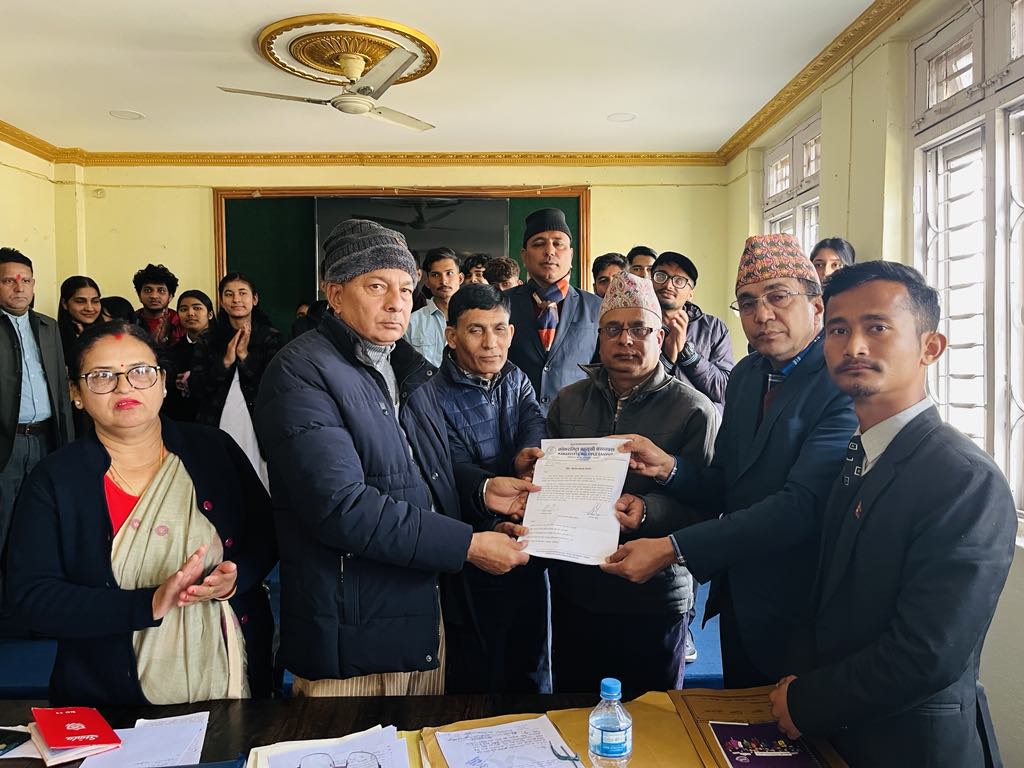 Mayor Baldev Singh Gomden Tamang and Sports Committee Chair Surendra Dhimal handing over a document to a representative, surrounded by attendees including a woman in a sari and various men in traditional and formal attire, inside a conference room with cream-colored walls and gold trim, natural daylight from windows.