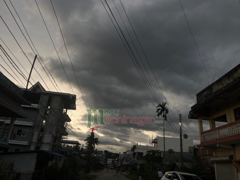 A gloomy street scene in a residential area with dark clouds overhead, power lines crisscrossing the sky, and buildings on either side of the road.