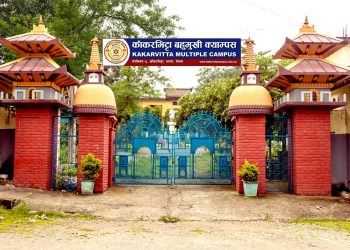 Kakarbhitta Multiple Campus entrance gate with blue metal doors and red brick pillars, surrounded by green trees and a cloudy sky.