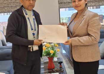 Laxmi Upreti, a program presenter of Surya TV and Media Pvt. Ltd., and Namrata Khadka, Operation Incharge of Hotel Ashwatth, are exchanging a collaboration agreement document. They are standing in a luxurious room with a coffee table between them, adorned with flowers. The setting appears to be indoors with natural daylight.