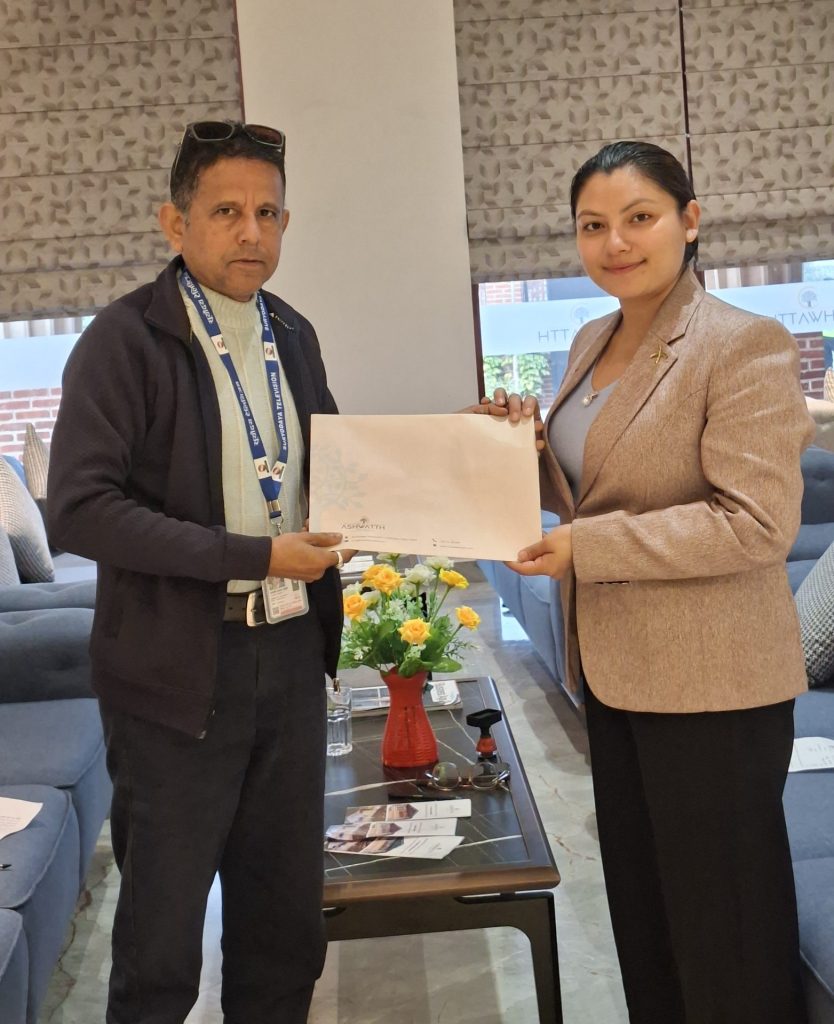 Laxmi Upreti, a program presenter of Surya TV and Media Pvt. Ltd., and Namrata Khadka, Operation Incharge of Hotel Ashwatth, are exchanging a collaboration agreement document. They are standing in a luxurious room with a coffee table between them, adorned with flowers. The setting appears to be indoors with natural daylight.