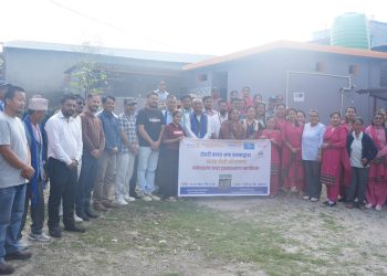 Group photo of attendees at the handover ceremony of a girl-friendly toilet at Priti Vidyalaya, Damak. Visible are Damak Mayor Ramkumar Thapa, Rotary Club of Damak President Kesav Kumar Agrawal, and other dignitaries. They are standing and smiling, holding a banner. The setting is outdoors with buildings in the background.