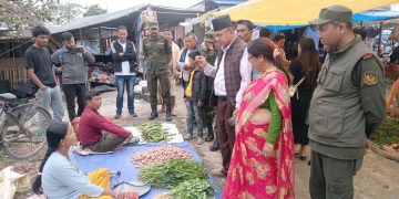 Mayor Gopal Chandra Budhathoki and Deputy Mayor Mina Pokhrel Upreti inspecting the Dhulabari market with officials and local vendors. They are standing near a table with vegetables and potatoes. The scene includes several people in casual and formal attire, with some taking pictures or observing.