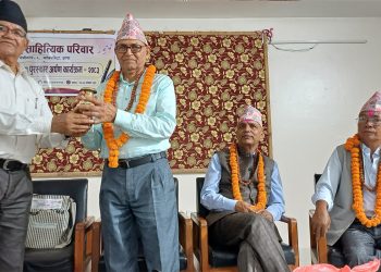 HONORING TRADITION: Renowned Nepali literary figures, from left, HOM SUWEDI, CHUDA MANI WASHISHT, GANGA PRASAD OFFICIAL, and another distinguished guest adorned in traditional Nepali attire, including Dhaka topi hats and marigold garlands, participate in a ceremonial event. They are seated and standing in a formal setting with a decorative backdrop, likely during a cultural or literary ceremony in Jhapa, Nepal.