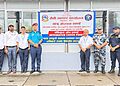 Group photo of officials from various agencies standing in front of a signboard for the Integrated Check Point at Kakarbhitta border crossing. Visible are (from left to right): a security officer in camouflage uniform, officials in plain clothes, and uniformed personnel from Nepal Police, Armed Police Force, and Nepal Customs. They are standing in front of a large sign with Nepali and English text. The scene is set on a concrete pavement outside a building with glass windows.