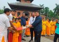 Men in traditional and casual attire handing over cricket equipment to young monks