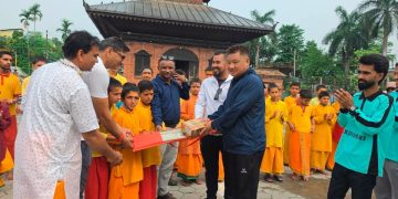Men in traditional and casual attire handing over cricket equipment to young monks
