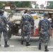 Armed police officers in camouflage uniforms inspecting a loaded cargo vehicle at a border checkpoint, with no specific individuals named in the image.
