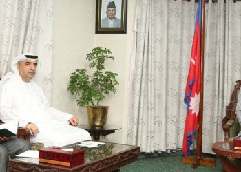 A meeting between Speaker of the House of Representatives, Dol Prasad Aryal, and UAE Ambassador to Nepal, Abdullah Jarwan Al Shamshi. The three men are seated in a formal setting with a wooden coffee table and chairs. Dol Prasad Aryal, wearing a light grey suit and a traditional Nepali hat, sits on the right. Abdullah Jarwan Al Shamshi, in a white robe and headscarf, sits in the middle. A third man in a grey suit sits on the left. The room features a framed portrait on the wall, a potted plant, and curtains.