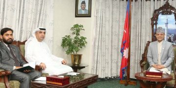 A meeting between Speaker of the House of Representatives, Dol Prasad Aryal, and UAE Ambassador to Nepal, Abdullah Jarwan Al Shamshi. The three men are seated in a formal setting with a wooden coffee table and chairs. Dol Prasad Aryal, wearing a light grey suit and a traditional Nepali hat, sits on the right. Abdullah Jarwan Al Shamshi, in a white robe and headscarf, sits in the middle. A third man in a grey suit sits on the left. The room features a framed portrait on the wall, a potted plant, and curtains.