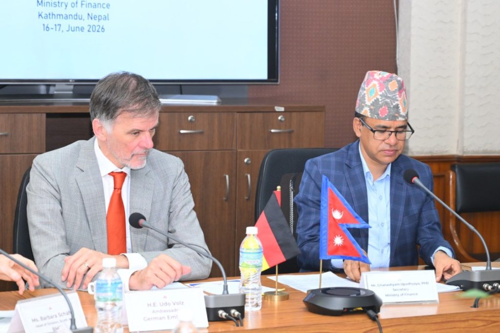 German Ambassador H.E. Udo Volz and Nepal's Ministry of Finance Secretary Mr. Ghanshyam Upadhyaya, PhD, sitting at a conference table with microphones, nameplates, and flags of Germany and Nepal, engaged in a meeting at the Ministry of Finance in Kathmandu, Nepal, on June 16-17, 2026.